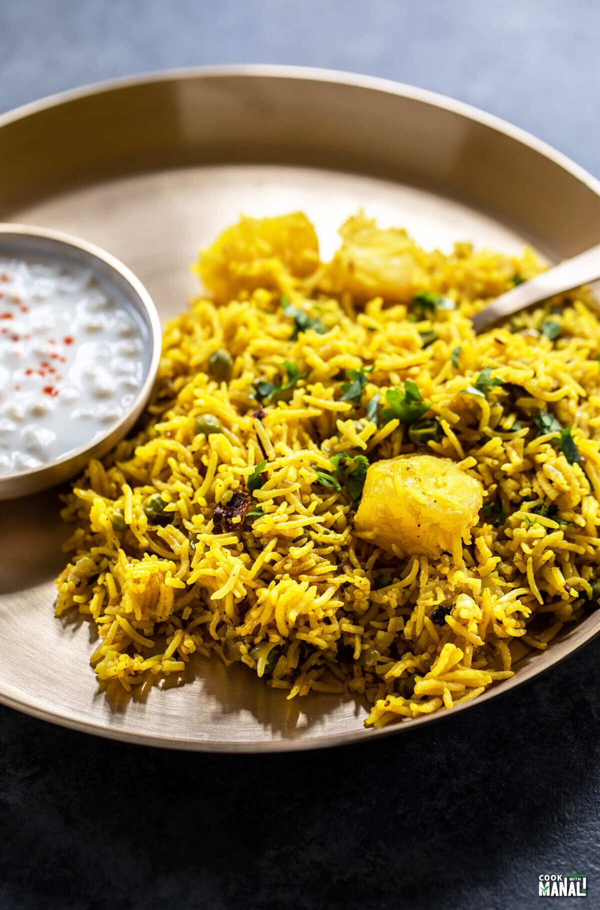 tehri served in a brass plate with a bowl of yogurt on side