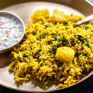 tehri served in a brass plate with a bowl of yogurt on side