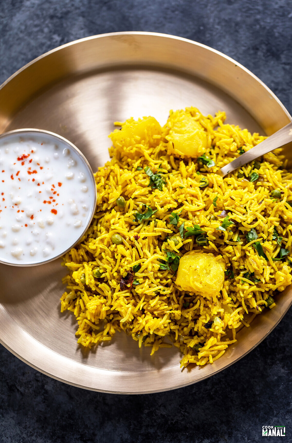 tehri served in a brass plate with a bowl of yogurt on side