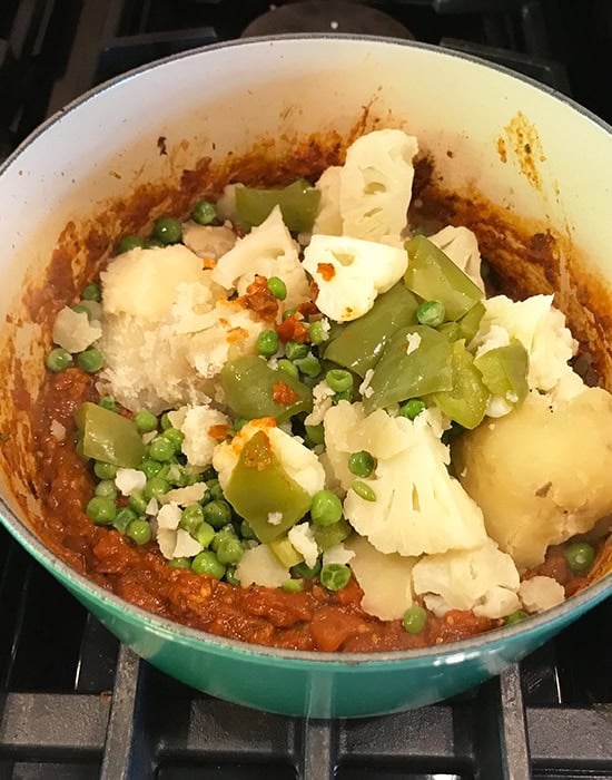 boiled vegetables added to a pot of masala
