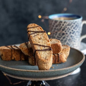 biscotti arranged on a plate with a cup of coffee placed in the background