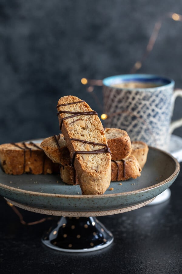 biscotti arranged on a plate with a cup of coffee placed in the background