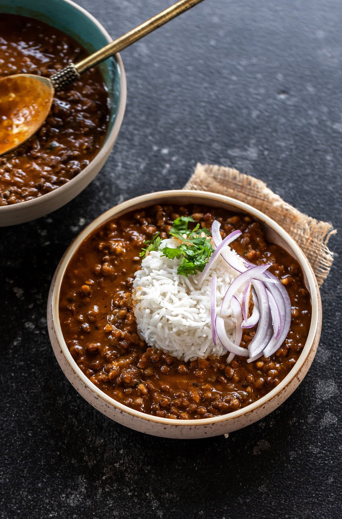 black lentils served with white rice in a bowl and topped with sliced onions and cilantro