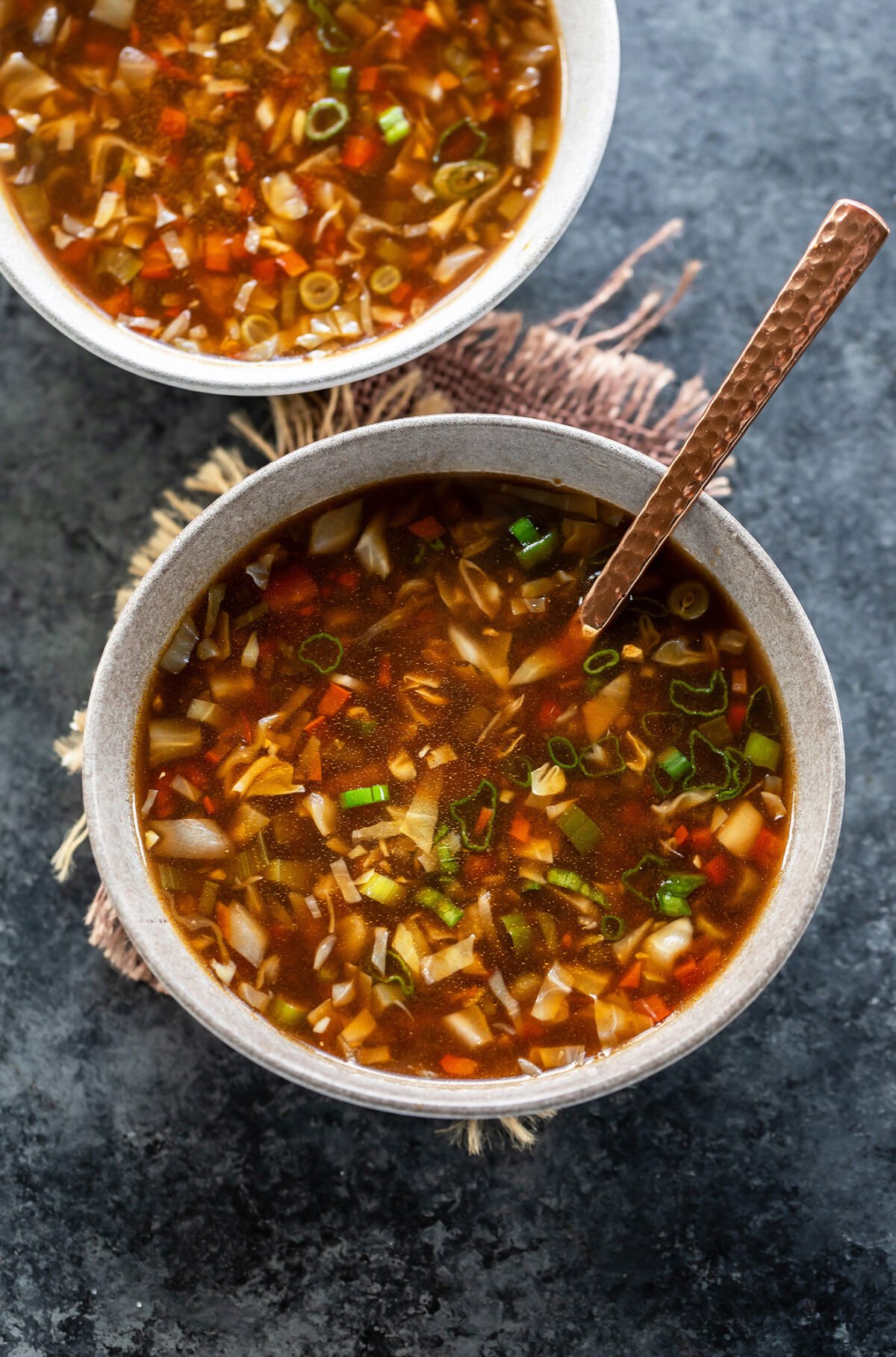 vegetable soup served in a white color bowl with a copper spoon