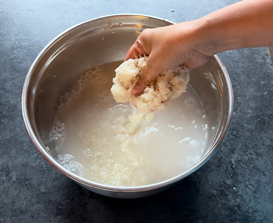 idli rice being washed with water in a steel bowl
