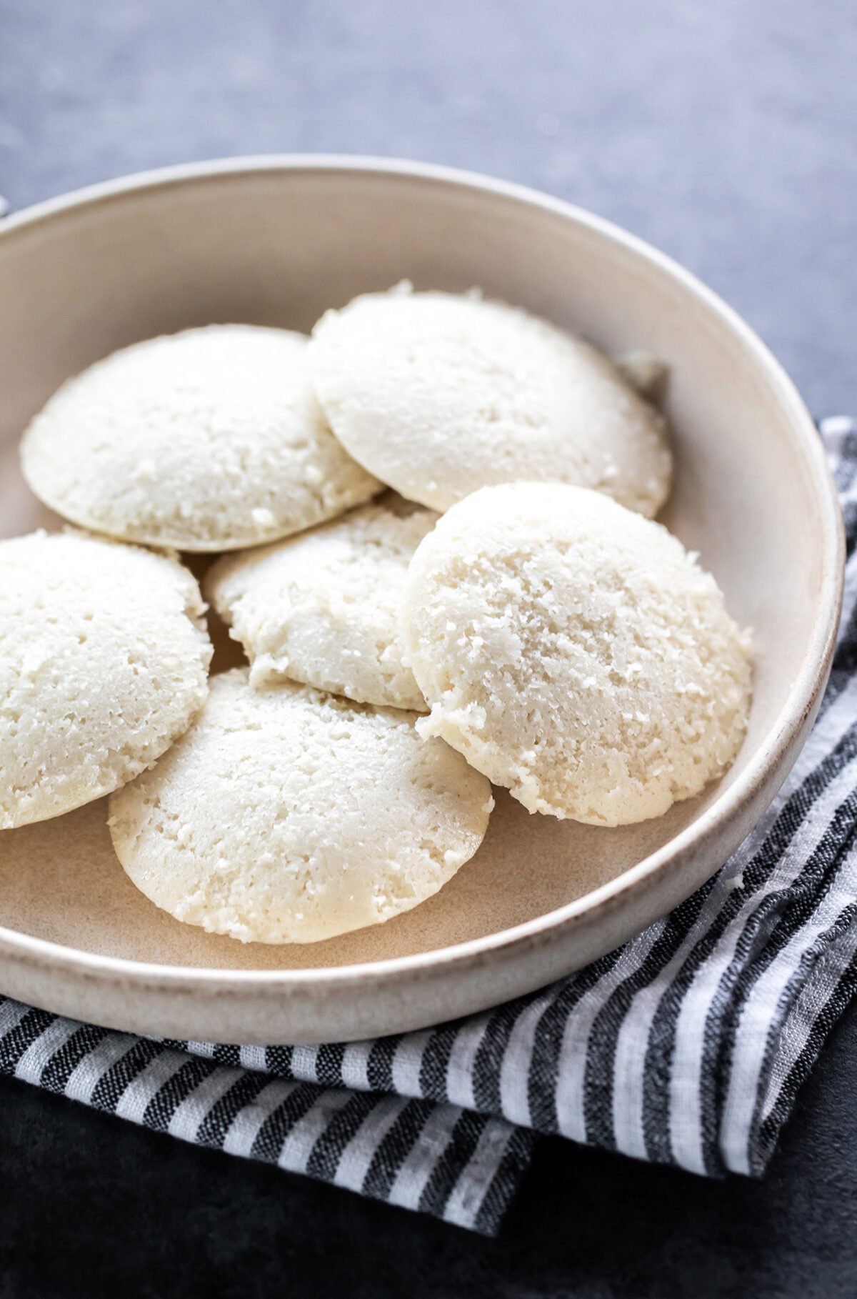 6 idlis served in a white round bowl with a linen towel placed at the bottom