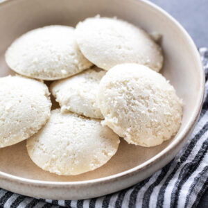 6 idlis served in a white round bowl with a linen towel placed at the bottom