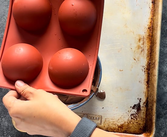 silicone mold being held upside down to shake all the excess chocolate from the mold