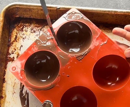scraping the excess chocolate from silicone mold using a spatula