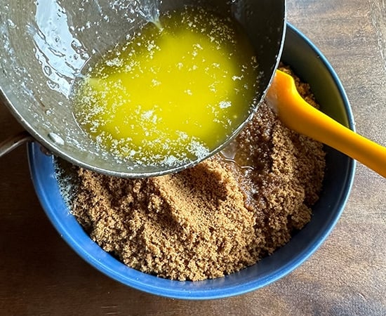 butter being added to a bowl of cookie crumbs