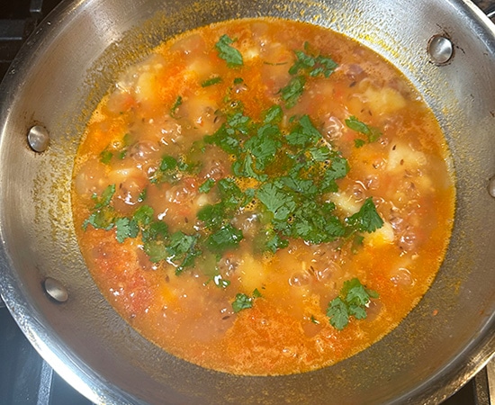 cilantro sprinkled on top of a curry in a kadai