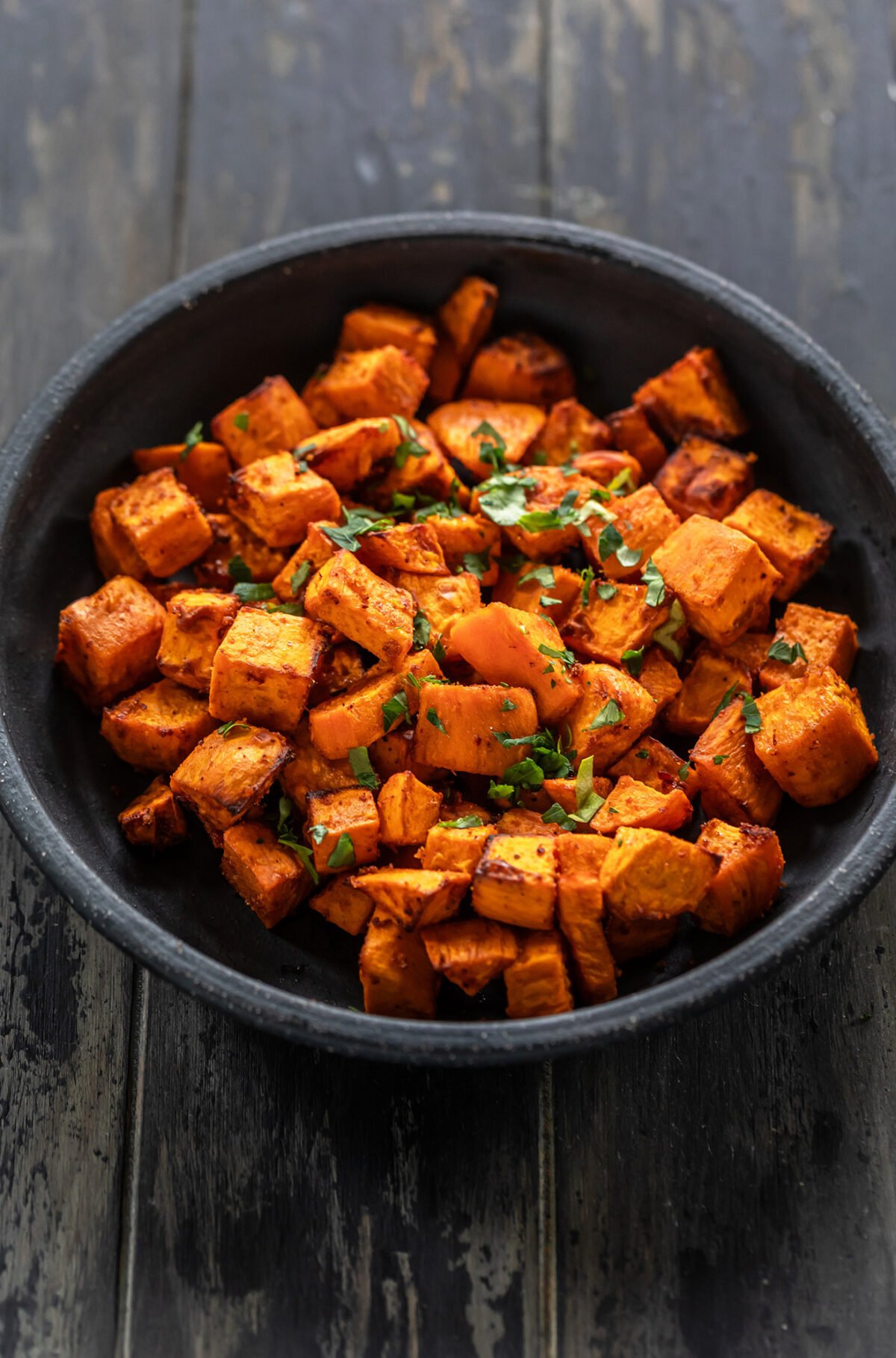 cubed roasted sweet potatoes in a black bowl with garnish of parsley