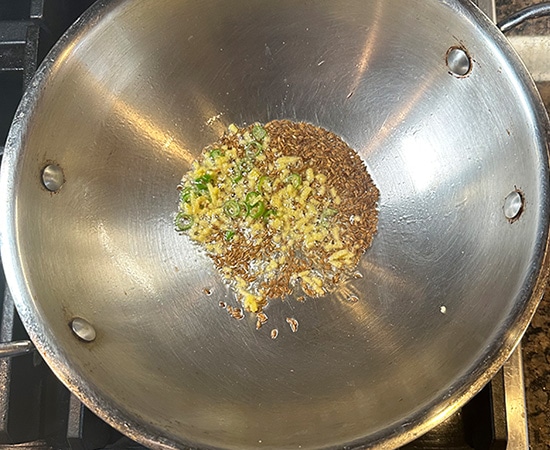 cumin seeds, ginger and chili sizzling in oil in a kadai