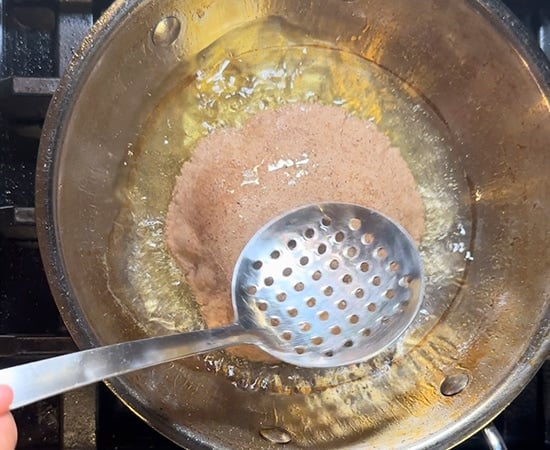 slotted spoon pouring oil over puri to puff it up