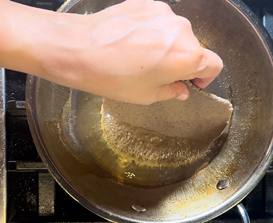 a hand dropping puri in hot oil in a kadai