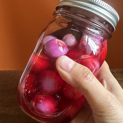 hand shaking a jar of pickled pearl onions