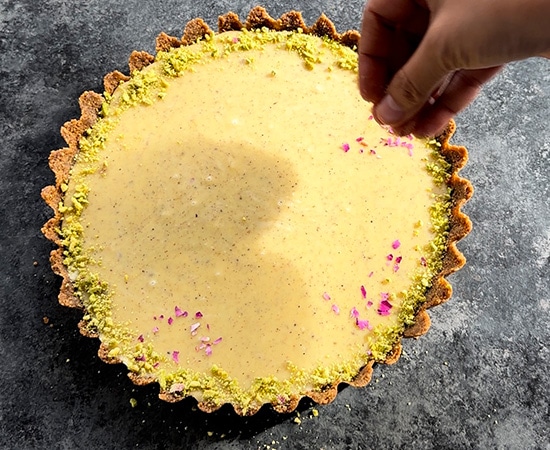 tart being decorated with crushed pistachios and rose petals