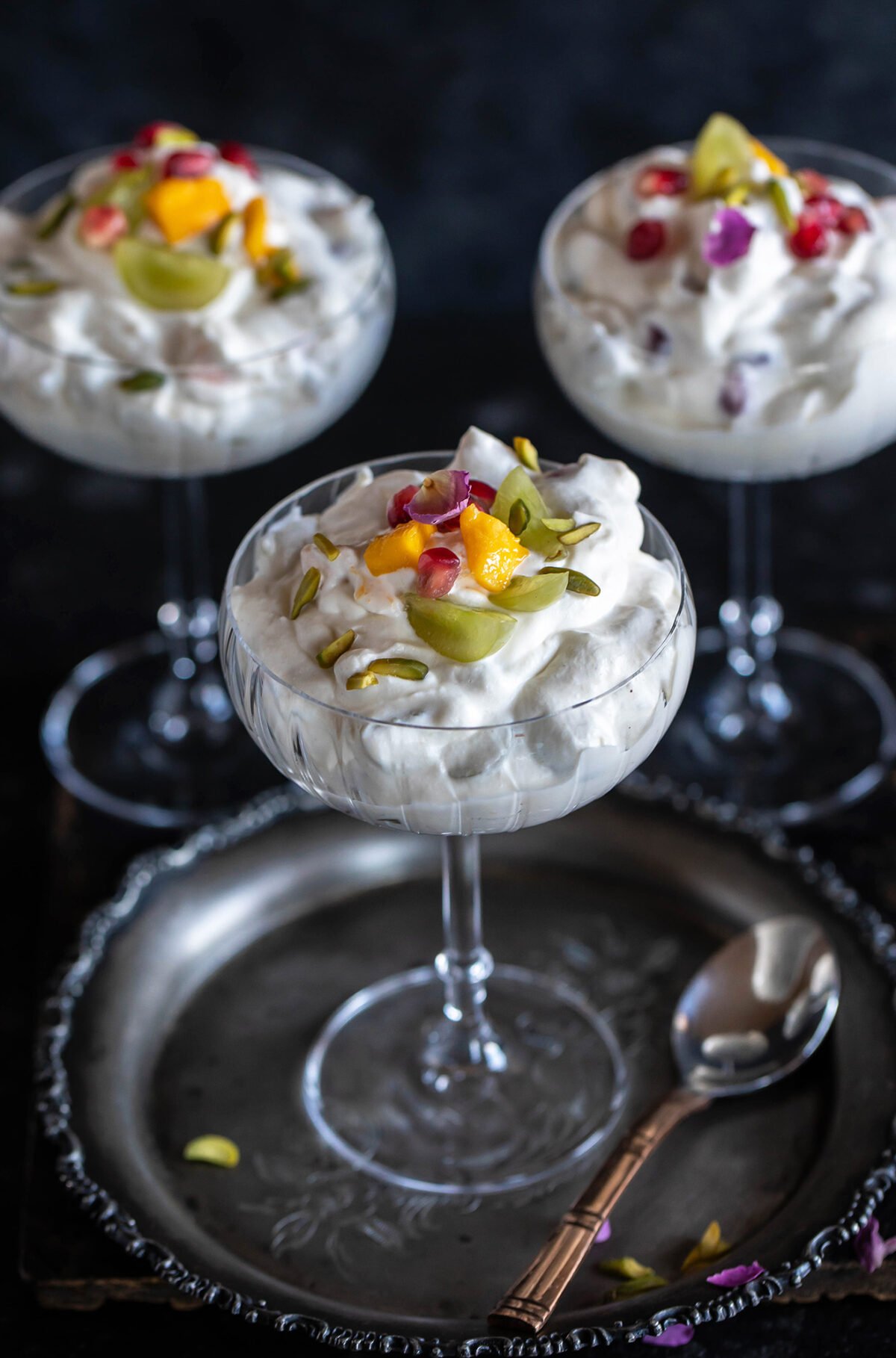 3 glass cups filled with whipped cream and fruits and garnished with rose petal