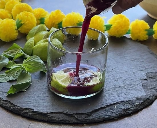 purple color drink being added to a glass with lime wedge