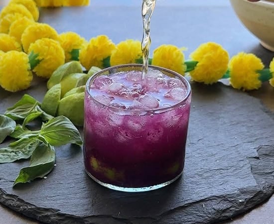 sparkling water being added to a glass filled with ice cubes and purple color drink