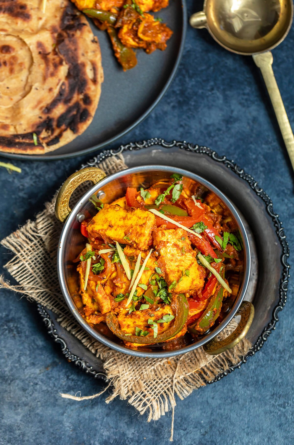 overhead shot of paneer jalfrezi served in copper kadai garnished with ginger juliennes and cilantro