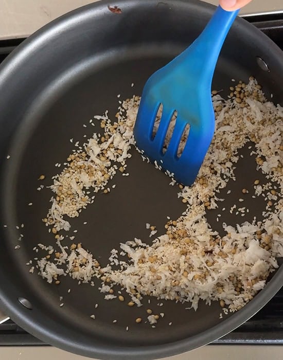 spices and coconut being roasted in a pan