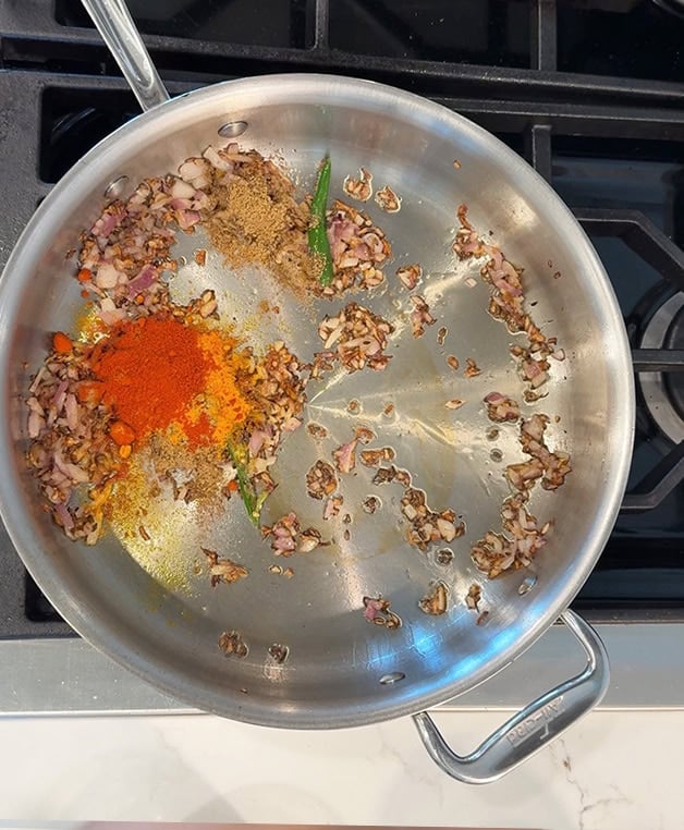 dry spices like turmeric, chili powder with onions and ginger in a steel pan
