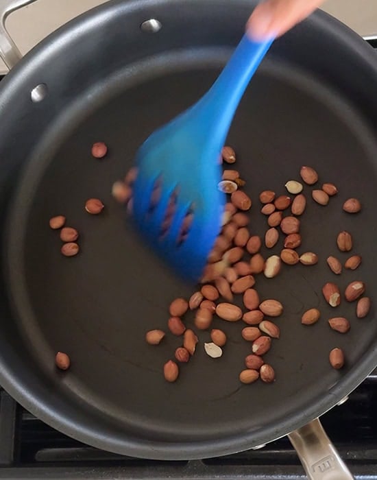 a blue spatula roasting peanuts in a pan