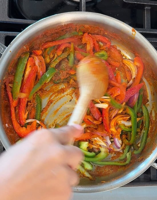 sliced peppers and onion being stirred in a steel pan with a spatula