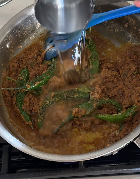 water being added to green chilies curry