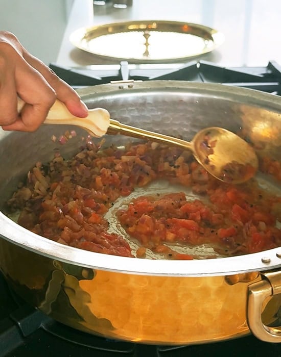 chopped tomatoes added to a pan and a spatula stirring the masala