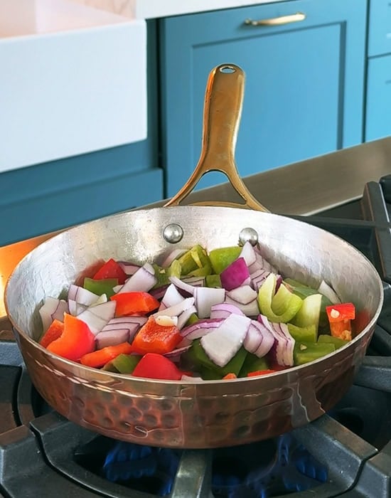 onions and peppers being pan fried in a copper pan