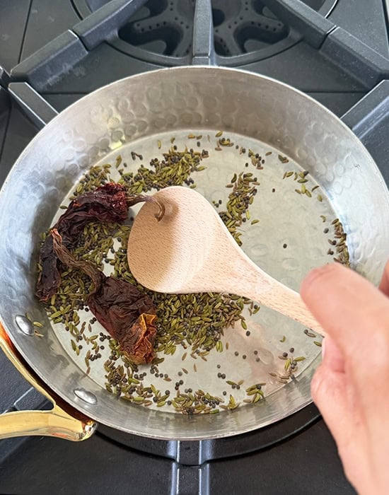 whole spices being sauteed in a pan with a wooden spatula