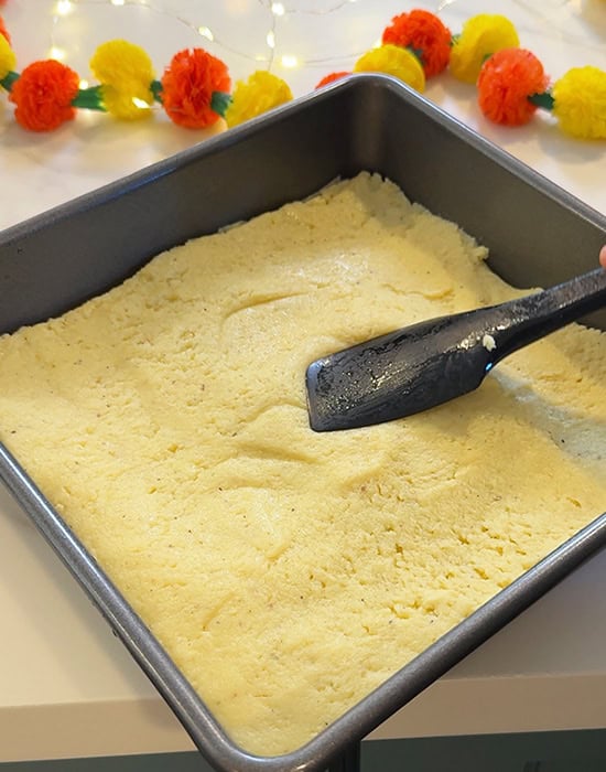 spatula pressing burfi mixture into a pan