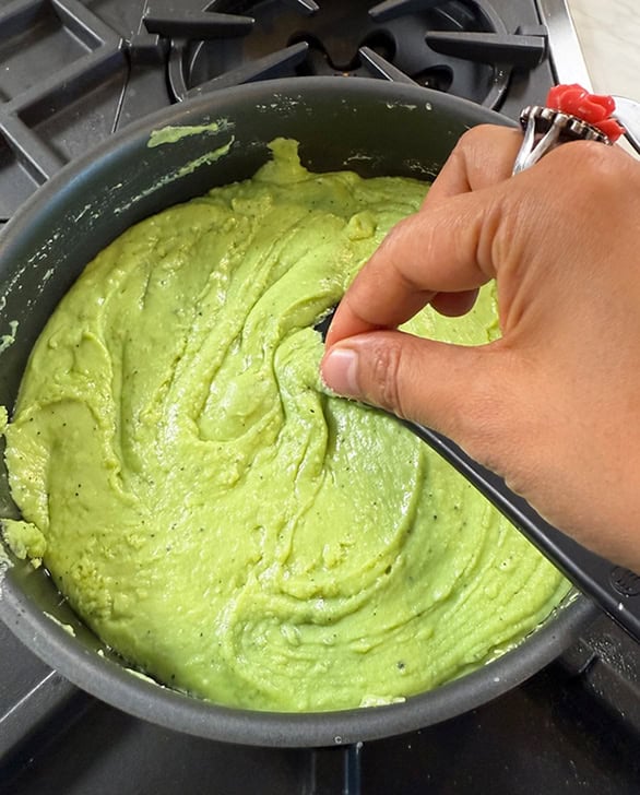 hand adding a pinch of something to a pan with burfi mixture