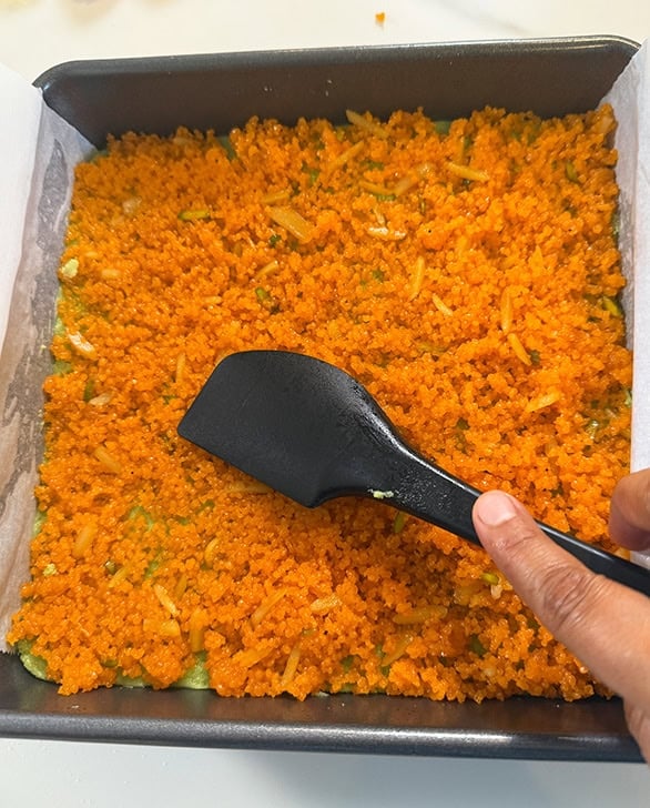 motichoor crumbles on top a pan being pressed with a spatula