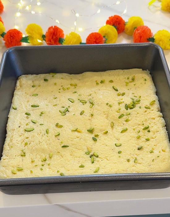 burfi in a square pan topped with slivered pistachios