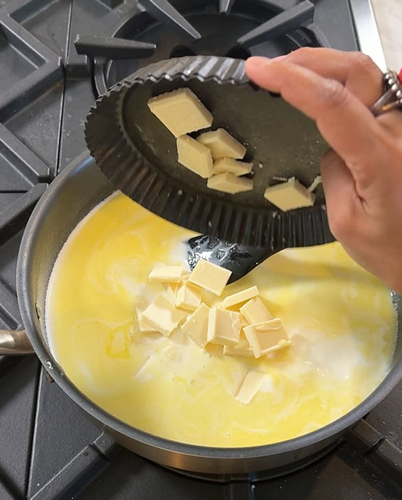 white chocolate being added to a pan with milk