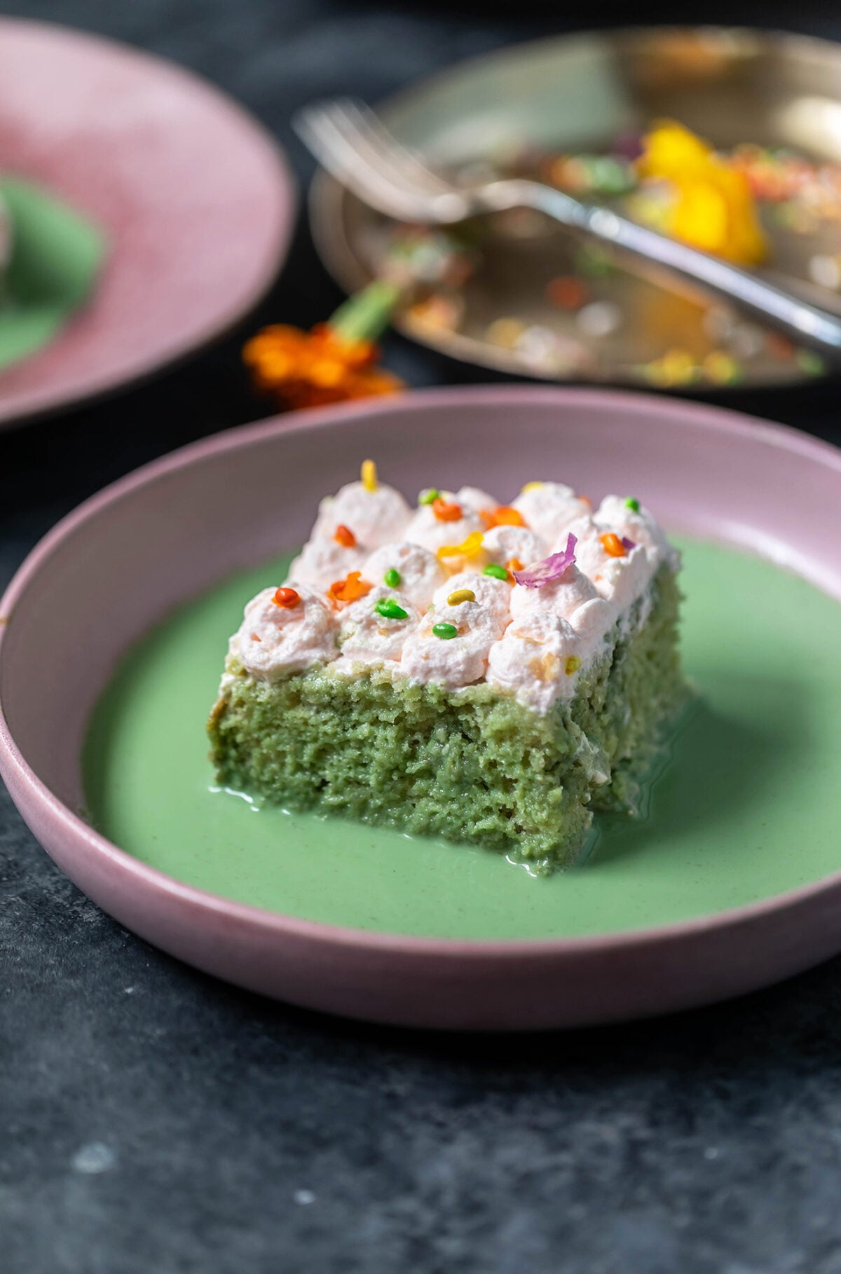 slice of cake in a pink color bowl with green color liquid poured around the cake