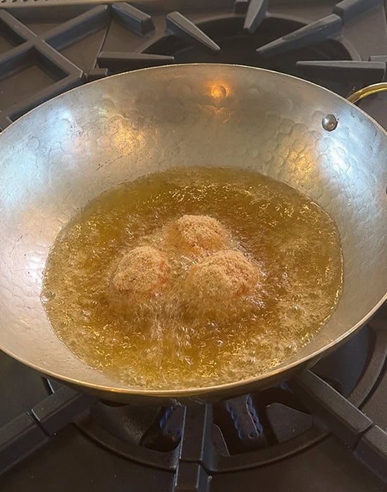 3 arancini being fried in hot oil