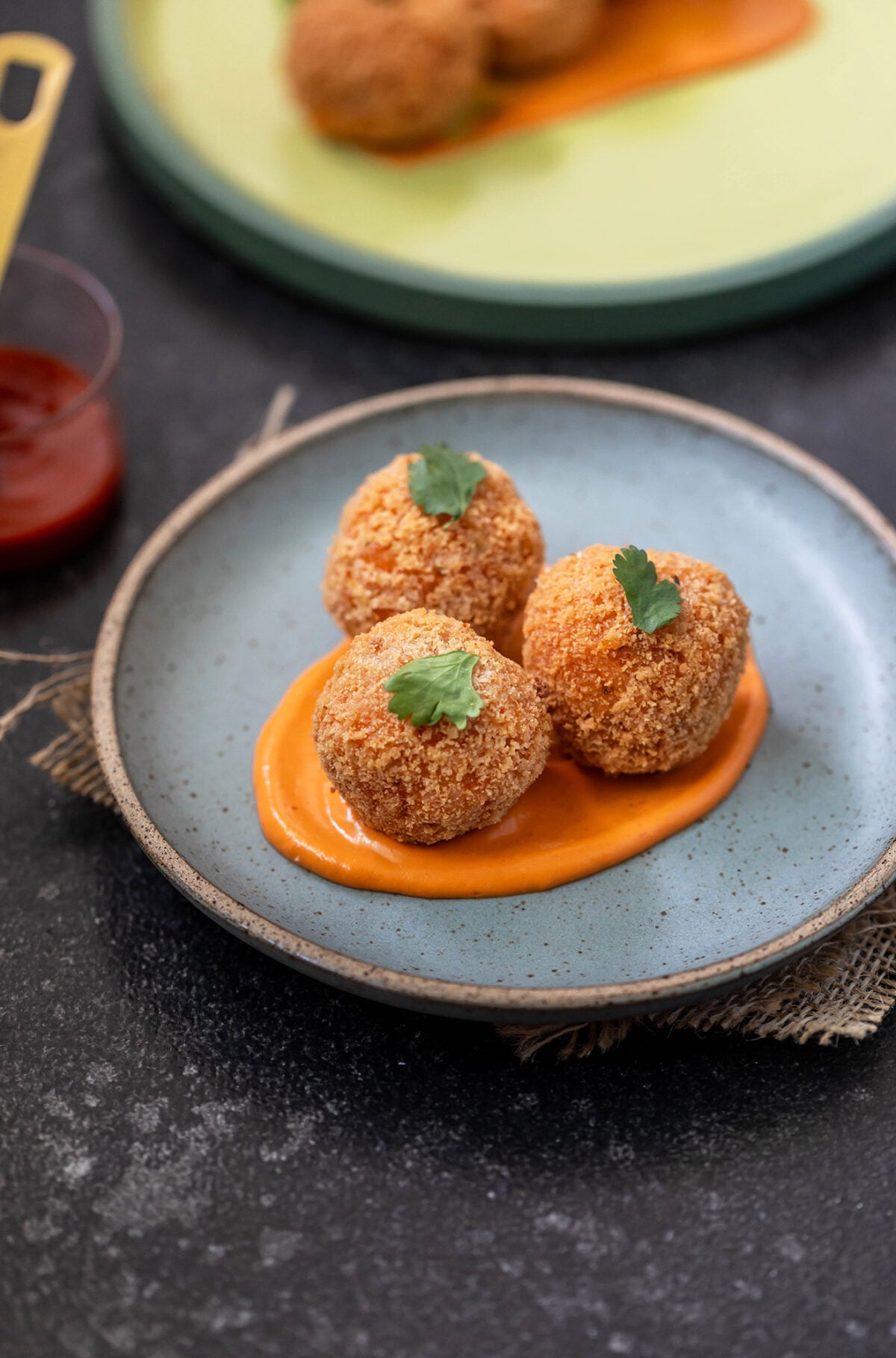 3 arancini served over sauce in a round blue plate, garnished with cilantro