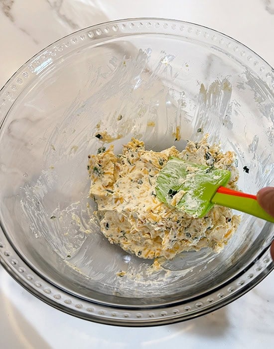 spatula mixing cheese with herbs in a bowl