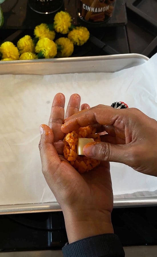 hand stuffing a cube of cheese inside rice ball