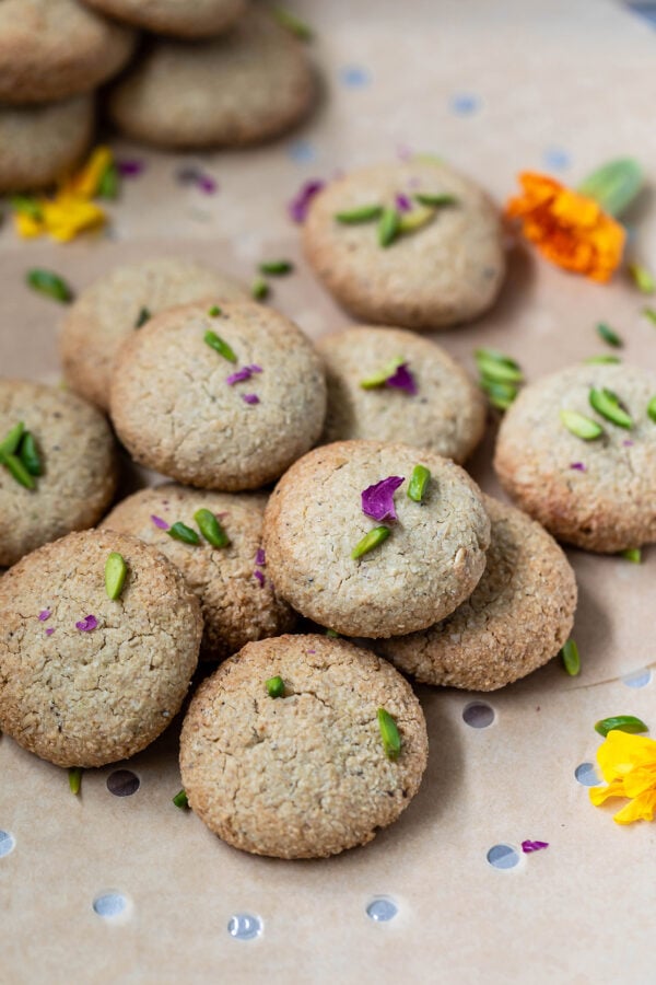 cookies garnished with rose petals and pistachios arranged on a baking sheet