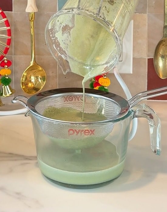 green liquid being strained into a glass jar using a strainer