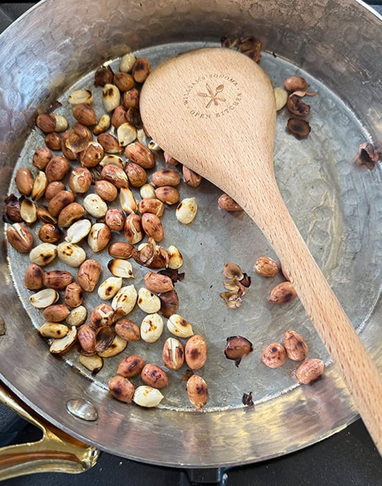 peanuts being roasted in a pan with a wooden spatula