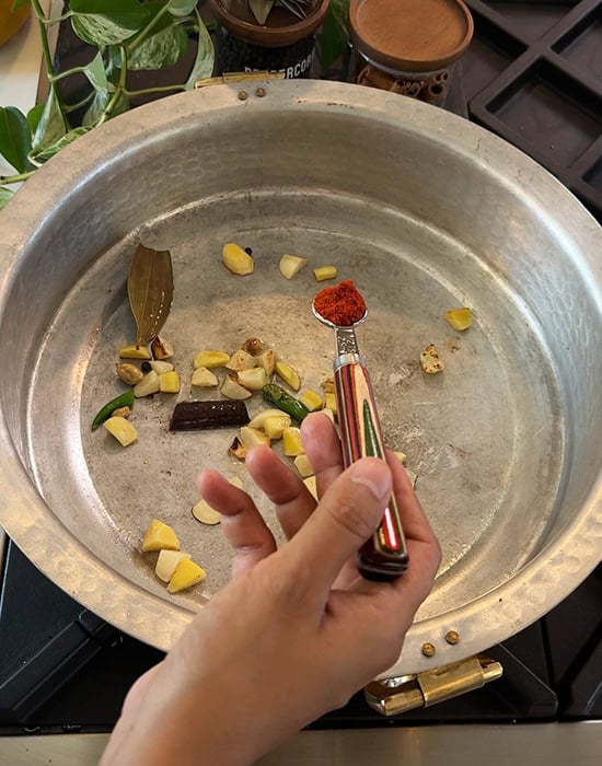 red chili powder being added to a pan with spices