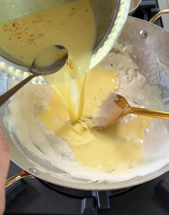 saffron milk being added to ricotta cheese in a kadai