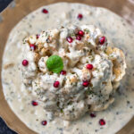 whole head of cauliflower in a white sauce garnished with pomegranate