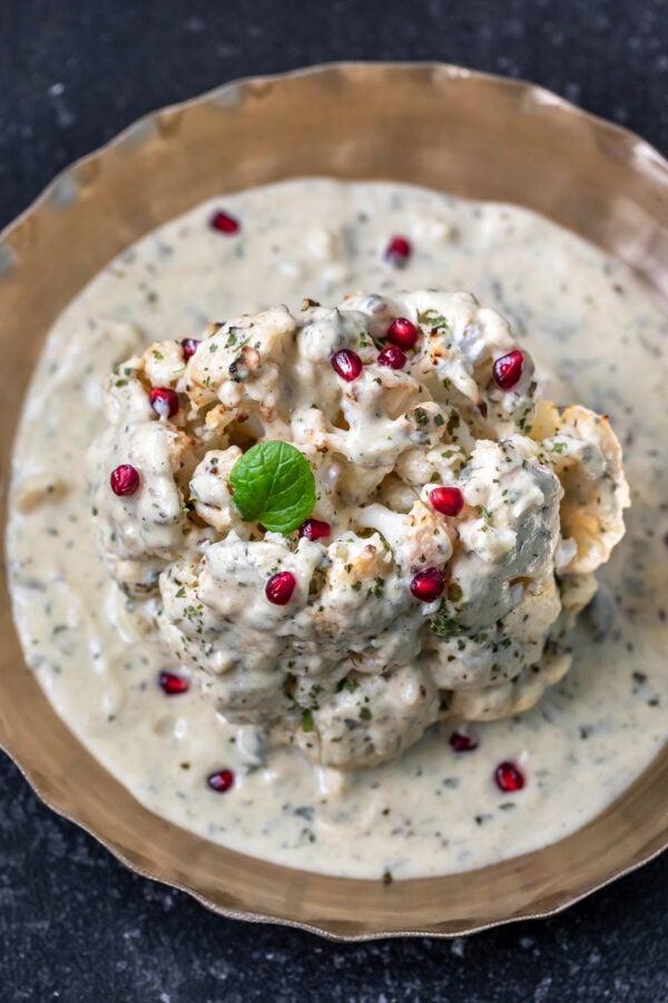 whole head of cauliflower in a white sauce garnished with pomegranate